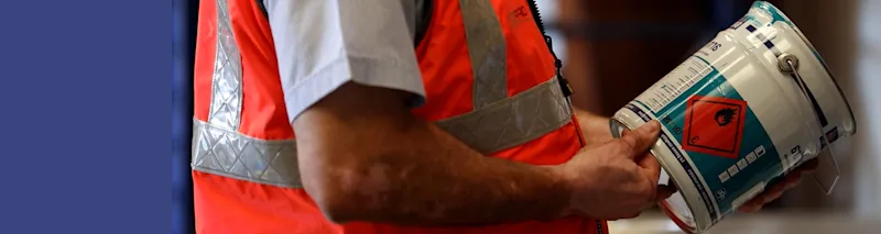 Un compagnon lit l'étiquette d'un pot de peinture